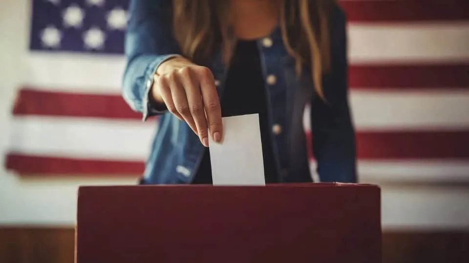 A hand placing a ballot into a voting box